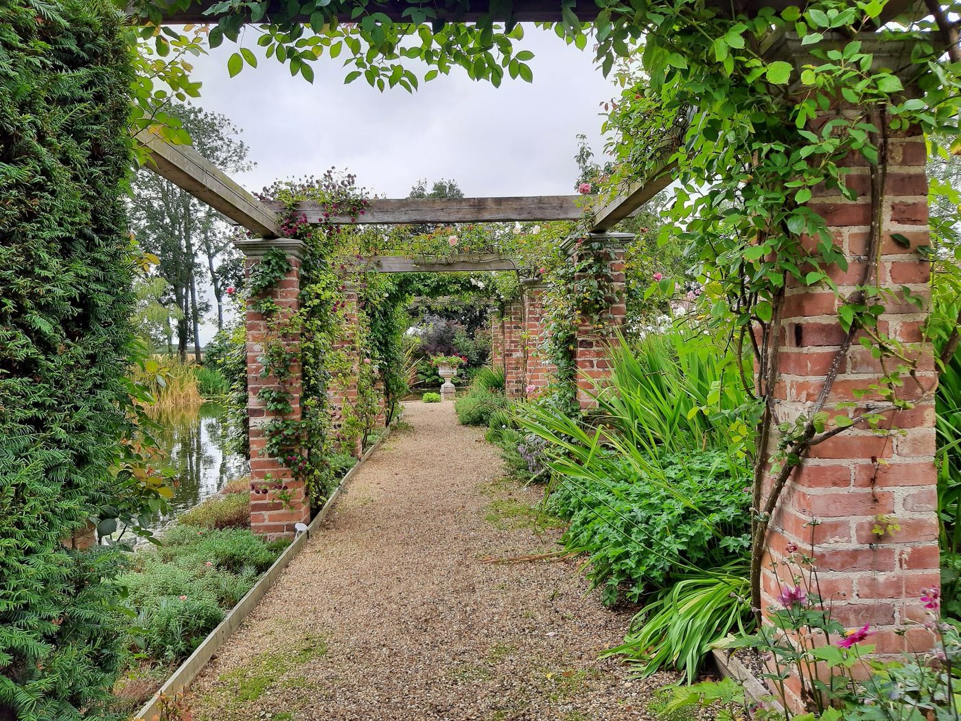A brick pergola over a gravel walk with deep planting either side, in an English garden