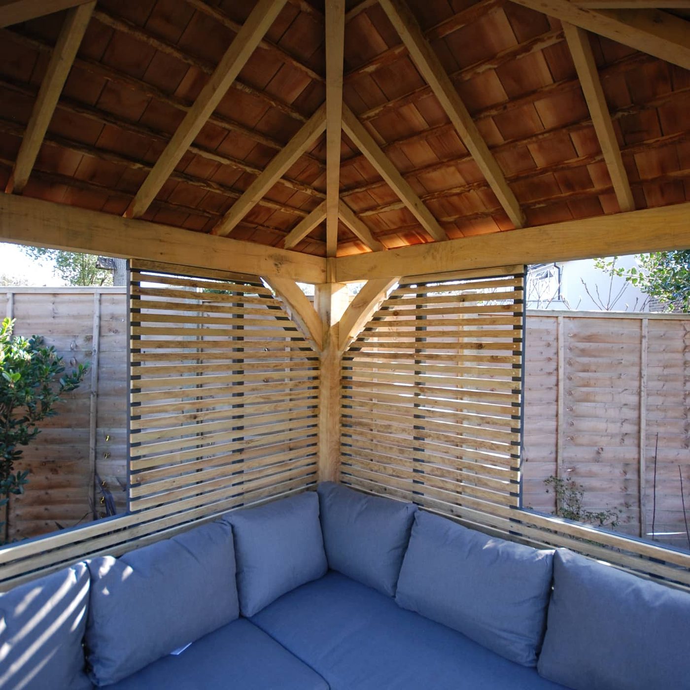 Inside the same building: exposed oak rafters, an oak-slat screen and a corner of seating — a dry, usable garden room rather than a shed with a window.